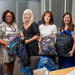 four WI members holding children's backpacks